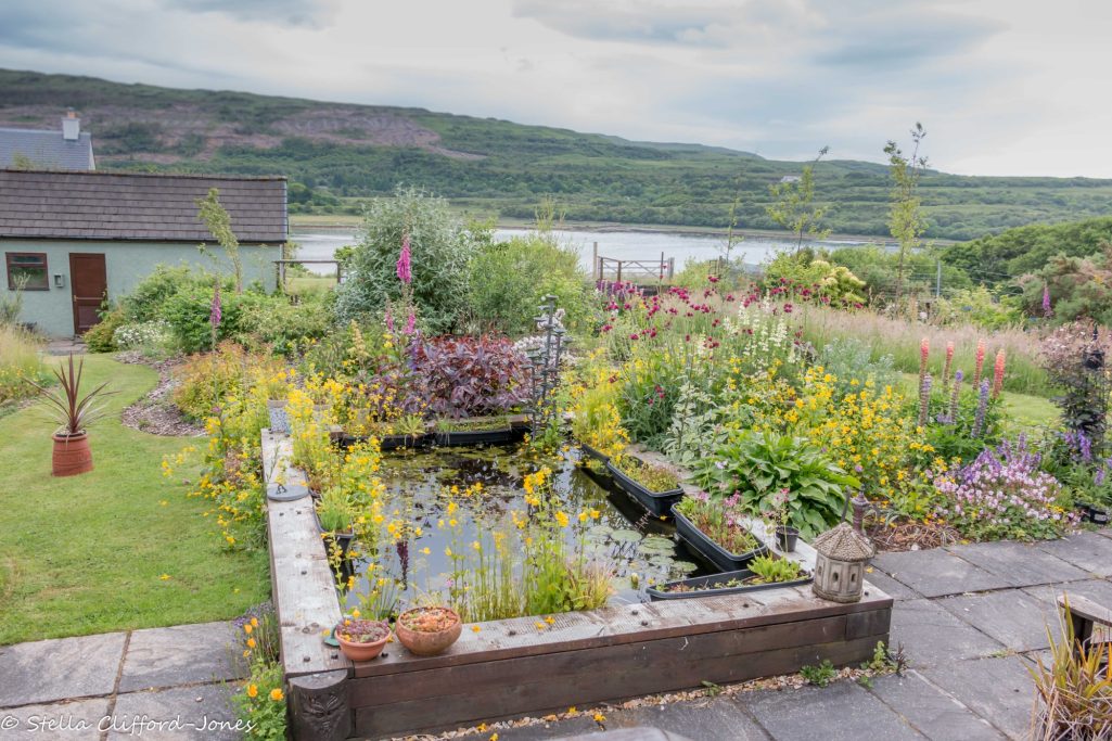 A raised pond made from sleepers surrounded by colourful planting.